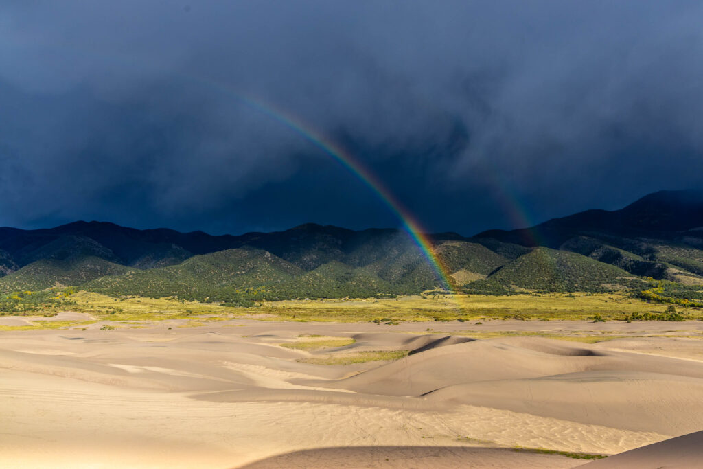 Rainbow over Great Sand Dunes with storm clouds and dune lines
