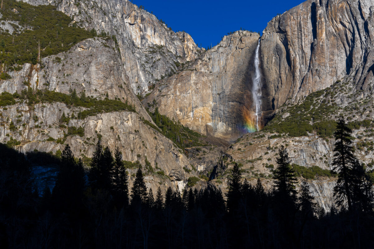 Close view of Yosemite waterfall with rainbow at base against granite wall