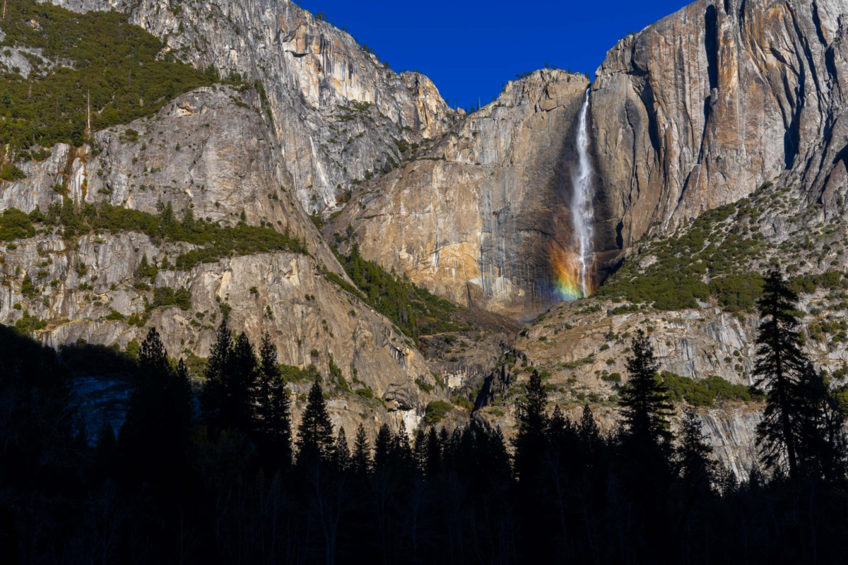 Close view of Yosemite waterfall with rainbow at base against granite wall