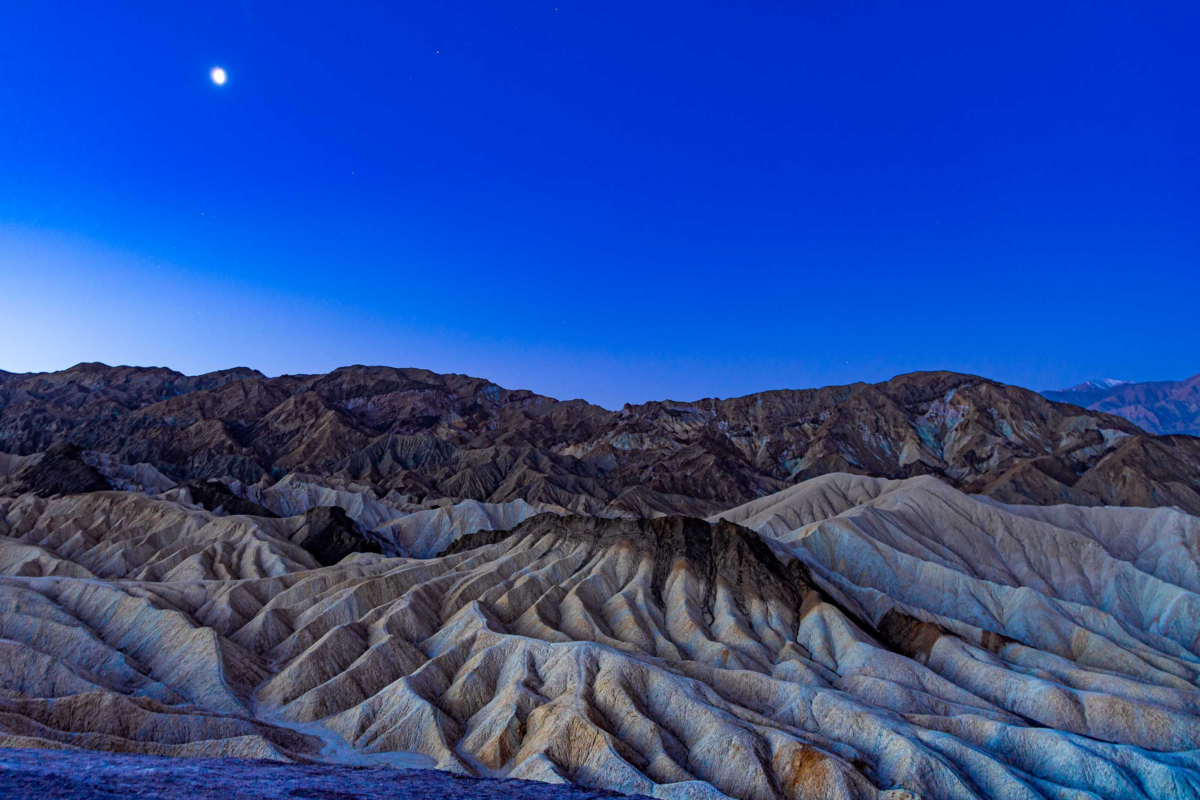 Moon above Zabriskie Point badlands at dawn in Death Valley National Park